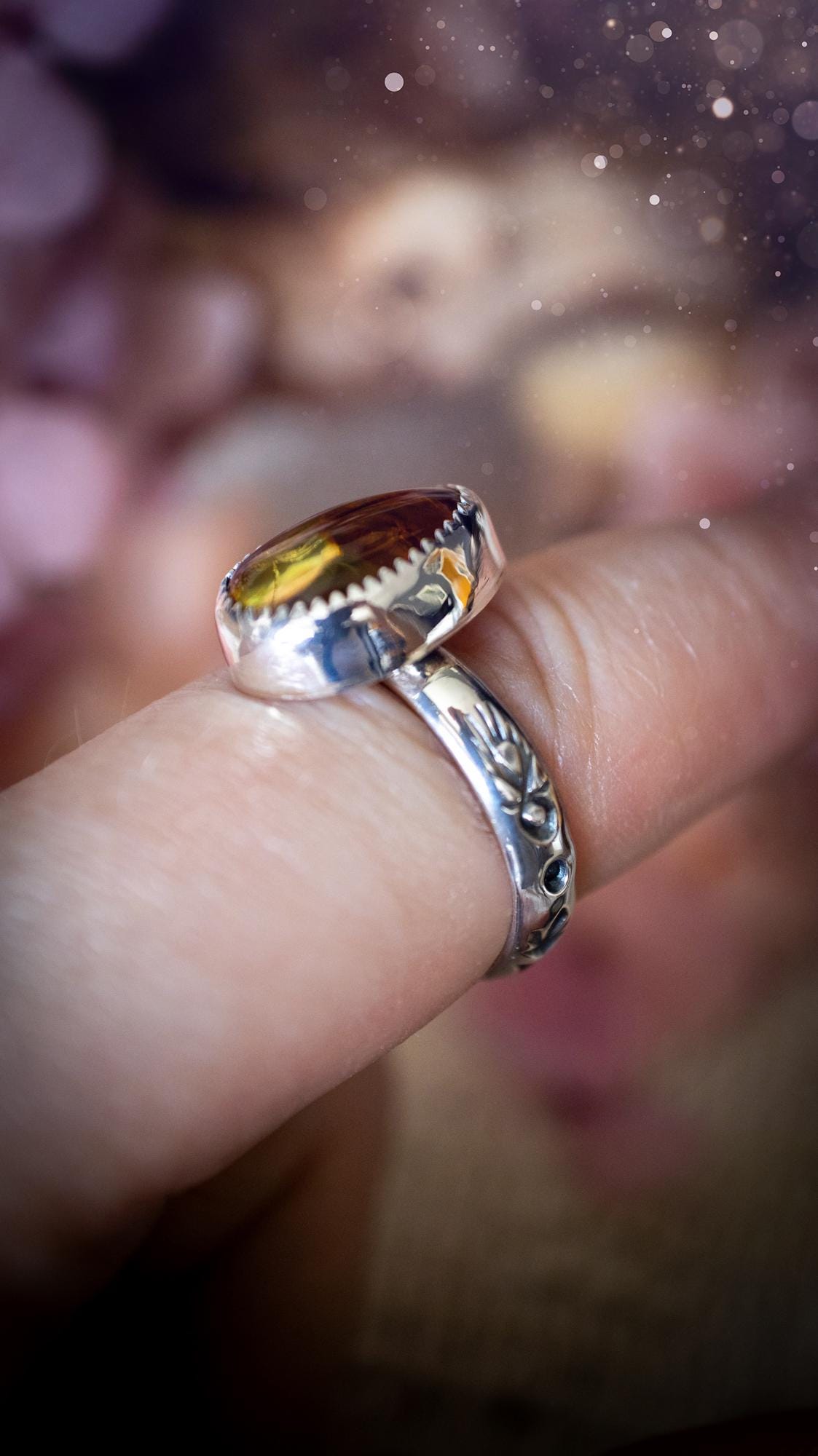 Handmade amber ring crafted from fine silver and sterling silver featuring a warm golden amber gemstone set in a decorative serrated bezel. The artisan ring showcases a signature patterned silver band with intricate detailing. Size UK O 1/2. A unique bohemian statement ring inspired by nature, displaying the rich honey tones and natural glow of genuine fossilised amber. Perfect handmade gemstone jewellery gift for crystal and silver jewellery lovers.