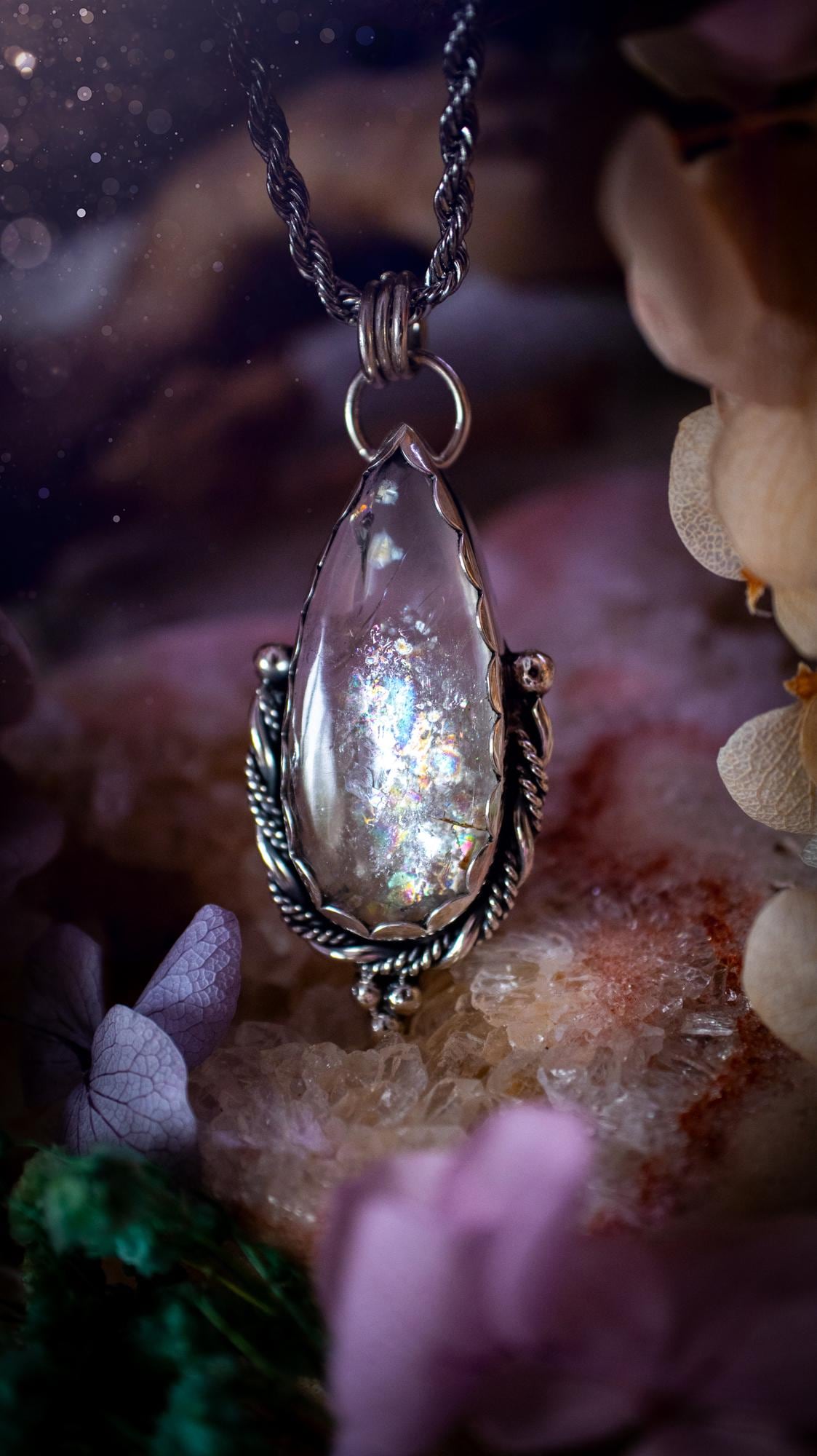 Handmade white topaz pendant necklace crafted from fine silver and sterling silver. The teardrop white topaz gemstone displays stunning natural cluster rainbows and subtle sparkle within the stone. The elegant silver setting highlights the crystal's unique inclusions and clarity. Photographed against a neutral background, this artisan gemstone necklace makes a thoughtful November birthstone gift. A necklace that is the definition of celestial and fairycore!