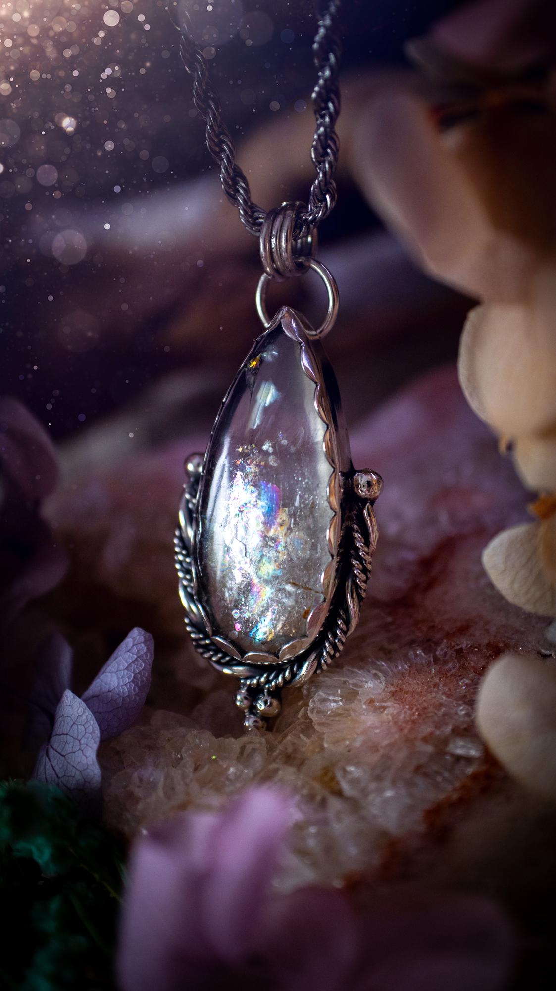 Handmade white topaz pendant necklace crafted from fine silver and sterling silver. The teardrop white topaz gemstone displays stunning natural cluster rainbows and subtle sparkle within the stone. The elegant silver setting highlights the crystal's unique inclusions and clarity. Photographed against a neutral background, this artisan gemstone necklace makes a thoughtful November birthstone gift. A necklace that is the definition of celestial and fairycore!
