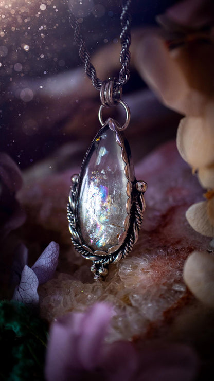 Handmade white topaz pendant necklace crafted from fine silver and sterling silver. The teardrop white topaz gemstone displays stunning natural cluster rainbows and subtle sparkle within the stone. The elegant silver setting highlights the crystal's unique inclusions and clarity. Photographed against a neutral background, this artisan gemstone necklace makes a thoughtful November birthstone gift. A necklace that is the definition of celestial and fairycore!
