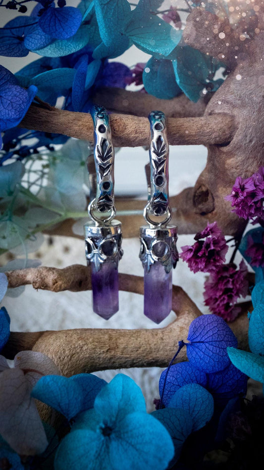 Handmade mini Amethyst point hoop earrings crafted from fine silver and sterling silver. Each natural purple Amethyst point is beautifully framed with ornate gothic gallery wire and suspended from hand-stamped sterling silver hoop earrings with textured detailing. Finished with secure butterfly backs, these artisan crystal earrings combine gothic, witchy and bohemian style. Elegant February birthstone jewellery, individually handcrafted with natural gemstones, making every pair completely unique