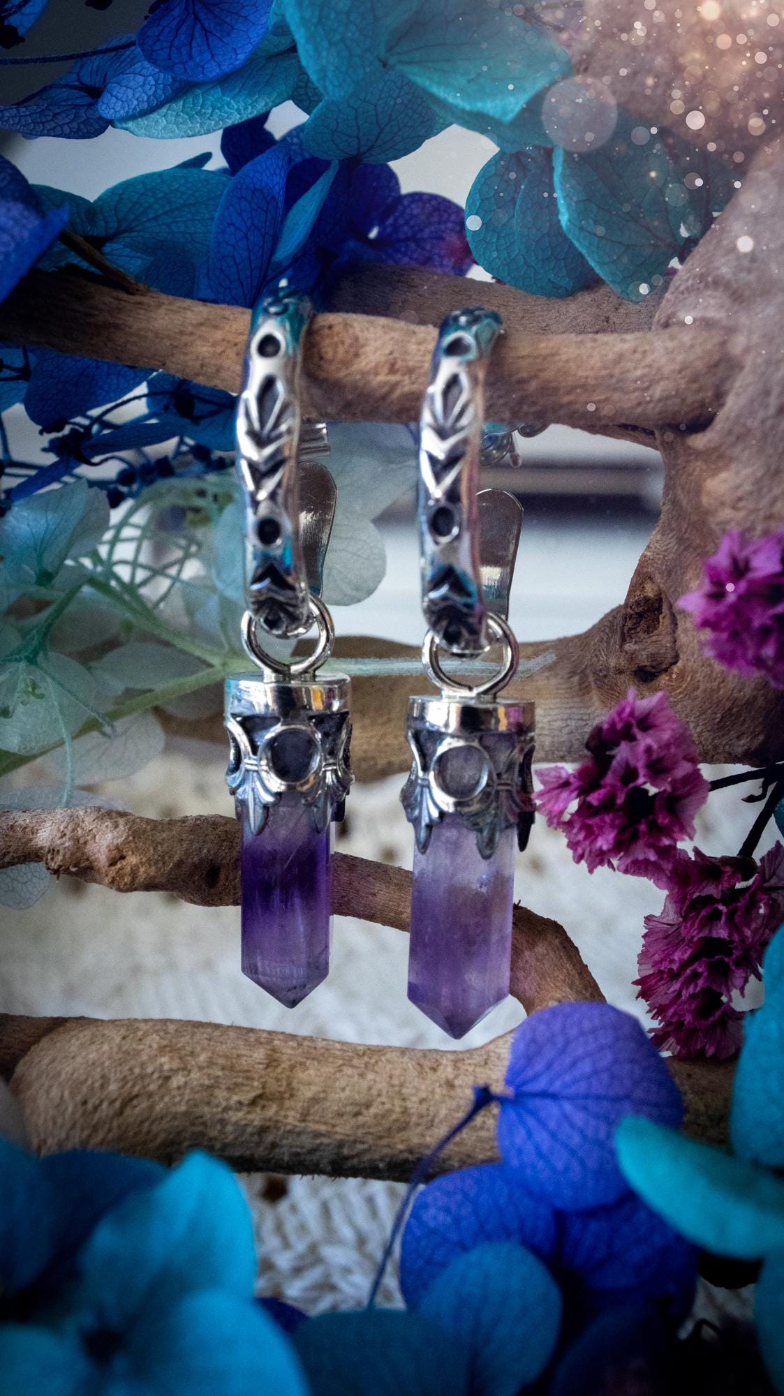 Handmade mini Amethyst point hoop earrings crafted from fine silver and sterling silver. Each natural purple Amethyst point is beautifully framed with ornate gothic gallery wire and suspended from hand-stamped sterling silver hoop earrings with textured detailing. Finished with secure butterfly backs, these artisan crystal earrings combine gothic, witchy and bohemian style. Elegant February birthstone jewellery, individually handcrafted with natural gemstones, making every pair completely unique