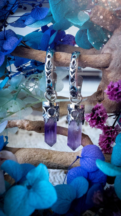 Handmade mini Amethyst point hoop earrings crafted from fine silver and sterling silver. Each natural purple Amethyst point is beautifully framed with ornate gothic gallery wire and suspended from hand-stamped sterling silver hoop earrings with textured detailing. Finished with secure butterfly backs, these artisan crystal earrings combine gothic, witchy and bohemian style. Elegant February birthstone jewellery, individually handcrafted with natural gemstones, making every pair completely unique